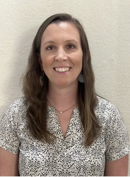 Woman with long brown hair smiling and wearing black and white patterned shirt.