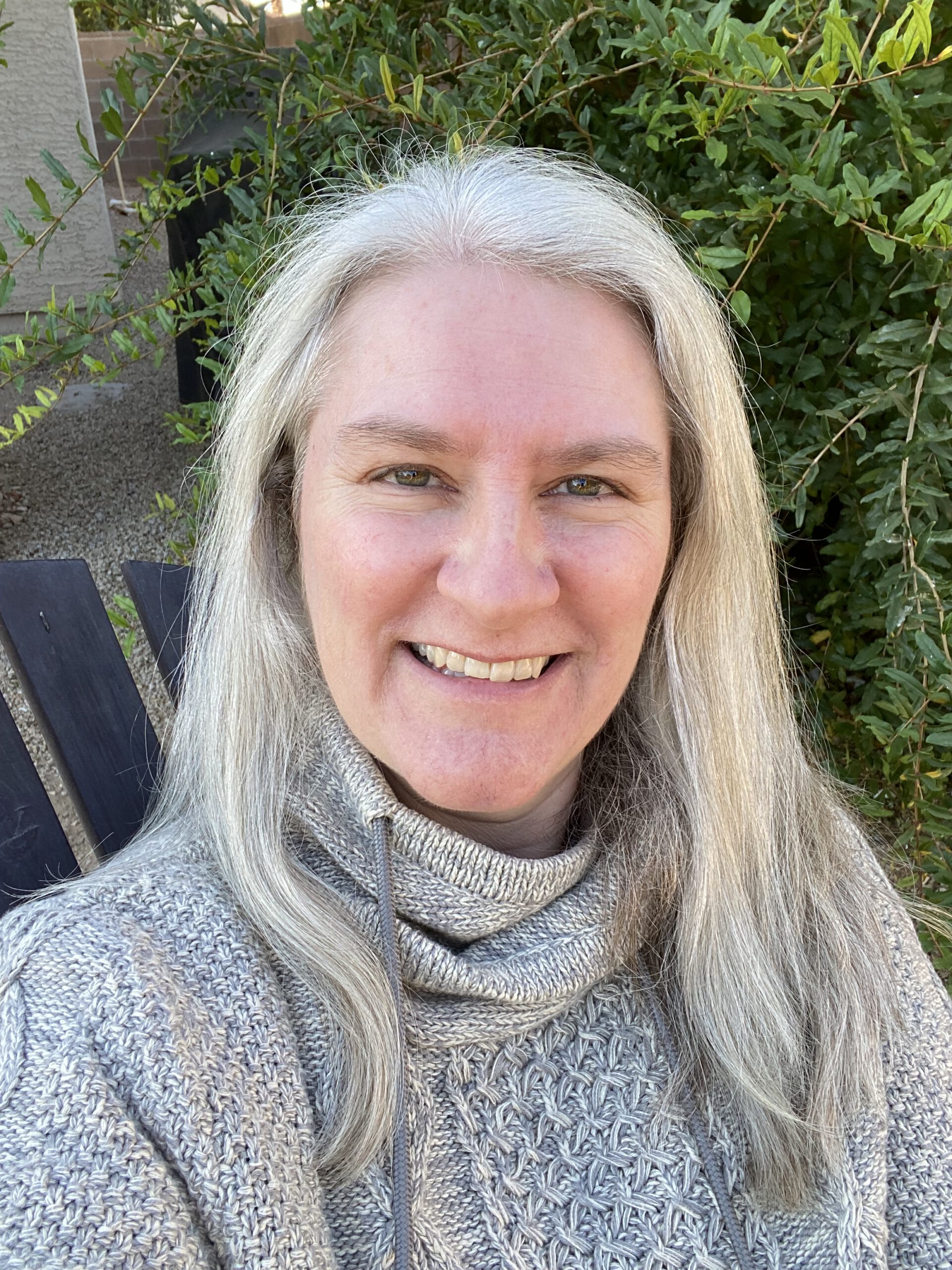 Woman with long grey hair smiling, wearing grey sweater.