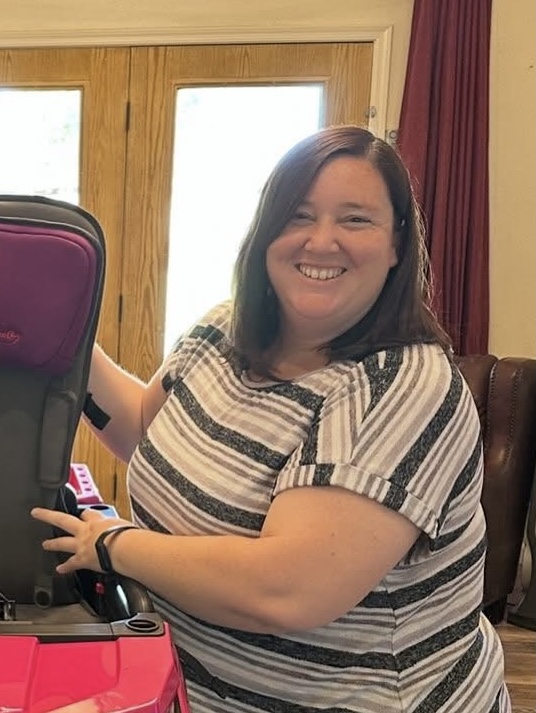 Dark haired woman smiling, wearing black and white horizontally striped shirt, with hands placed on adapted car. 